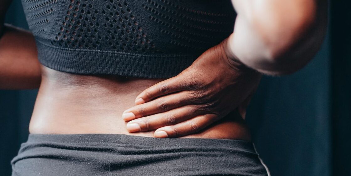 Prenatal Massage in Golden, CO An adult of African descent holding their lower back in pain, indicating discomfort or injury.